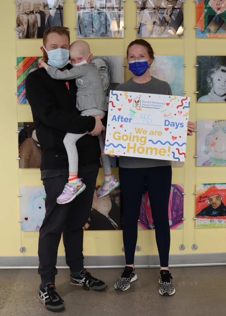 Father holding his child next to mother who is holding a sign that says "going home after 46 days"